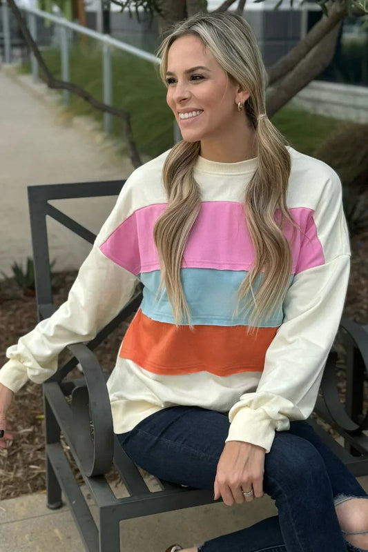 Woman wearing a colorblock sweatshirt with pink, blue, and orange stripes, seated outdoors