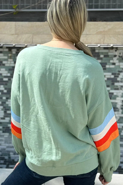 Woman wearing a sage green sweatshirt with colorful striped sleeves outdoors
