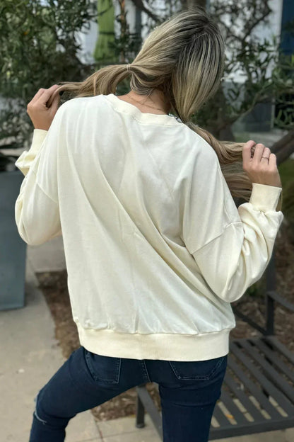 Woman outdoors in relaxed ivory pullover sweater and dark jeans, back view